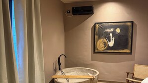 Un baño moderno con un lavabo de piedra, aire acondicionado de pared y una obra de arte abstracta.