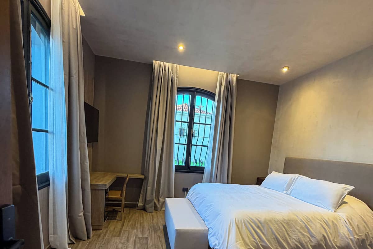 Un dormitorio con cama, escritorio, banca y ventana con cortinas.