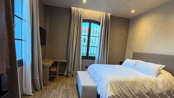 A bedroom with a bed, a desk, a bench, and a window with curtains.