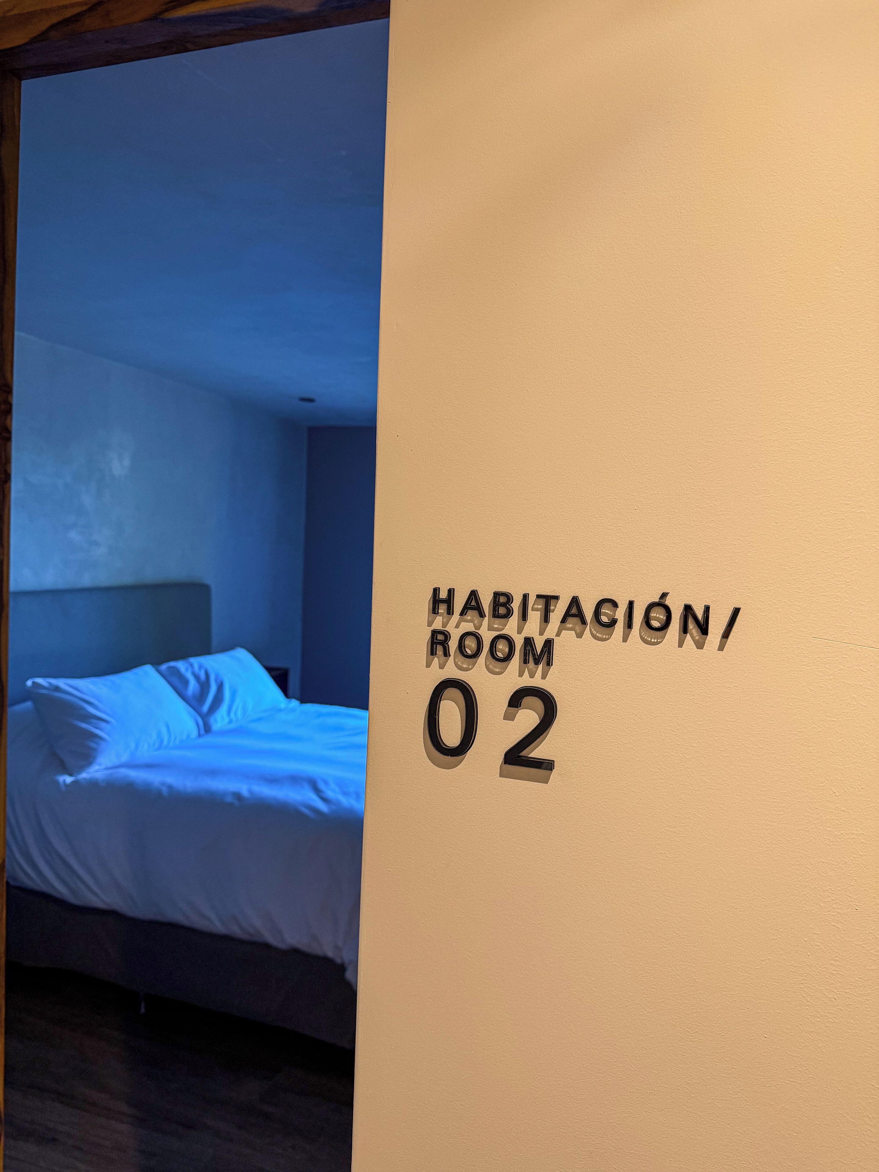 Una habitación con una cama y un letrero en la pared que indica 'HABITACIÓN/ROOM 02'.
