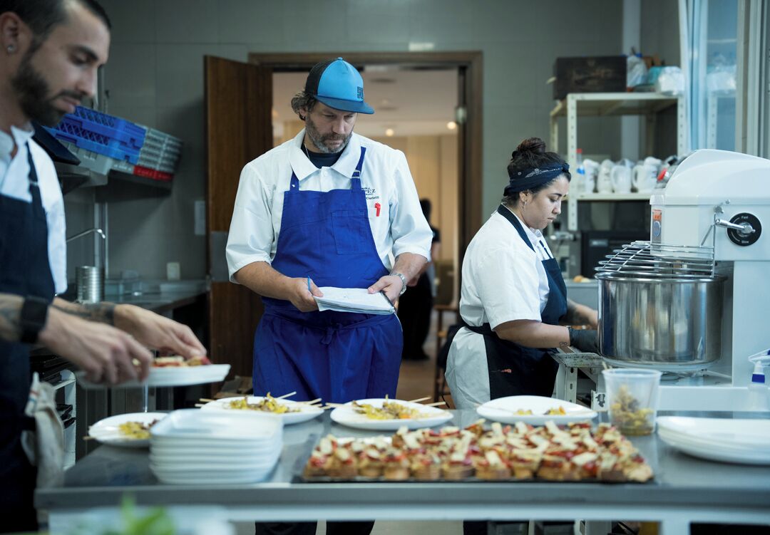 A kitchen area with chefs preparing food, a large pizza on the counter, and kitchen equipment.