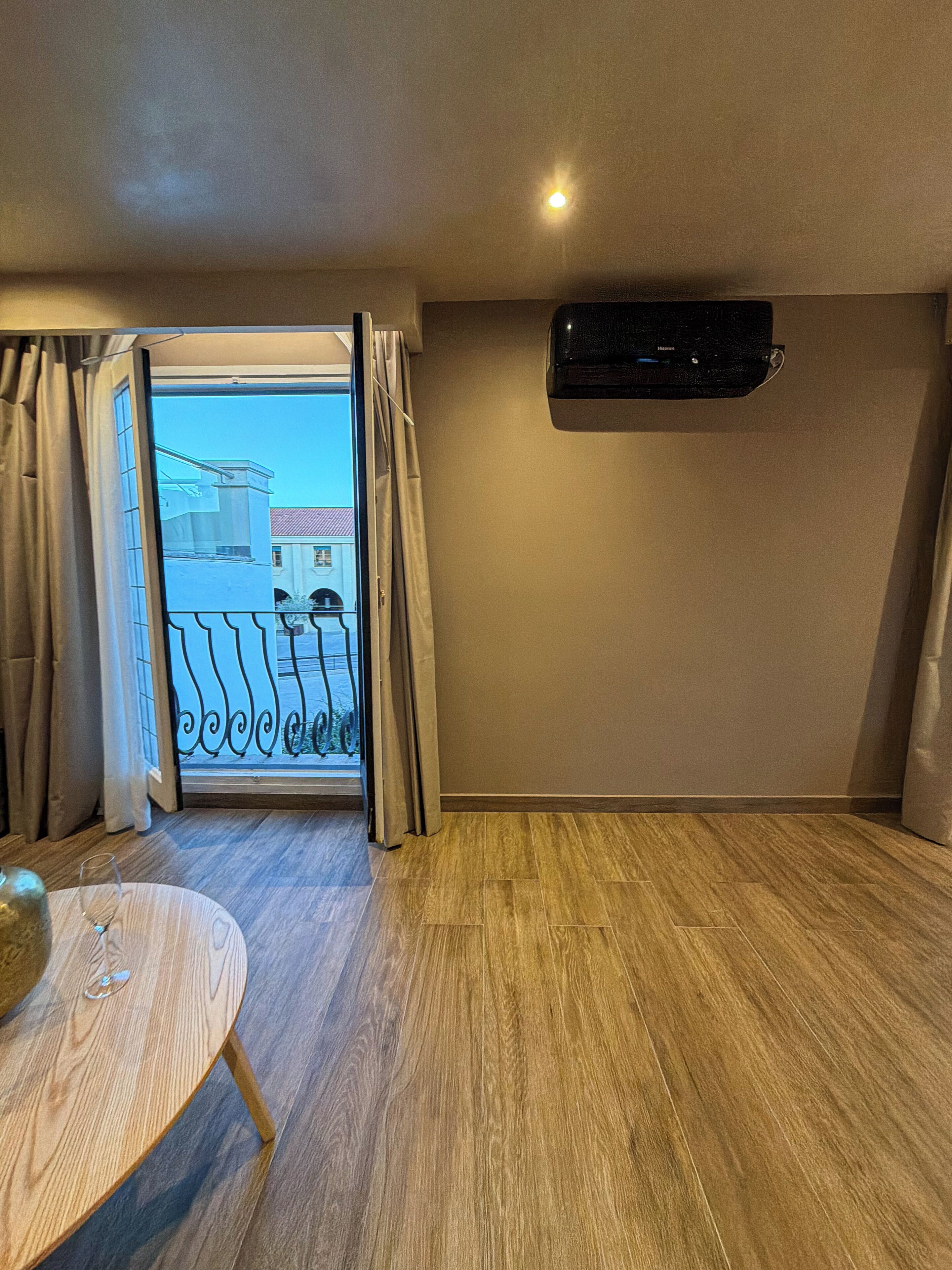 A room with a wooden floor, a table with a glass, and a view through a door to a balcony.