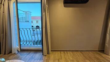 A room with a wooden floor, a table with a glass, and a view through a door to a balcony.
