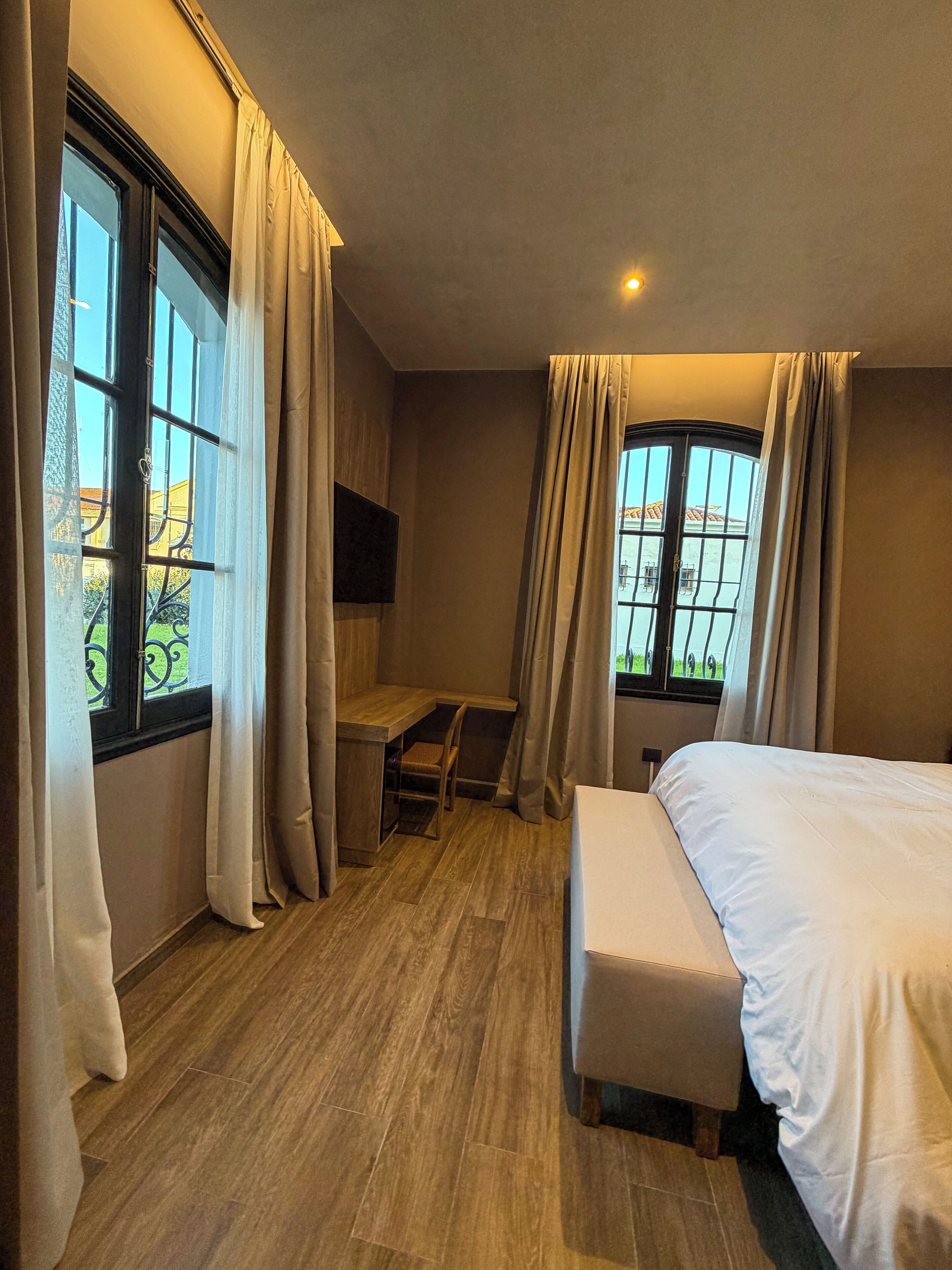 Una camera d'albergo con un letto, una scrivania e due finestre con tende.