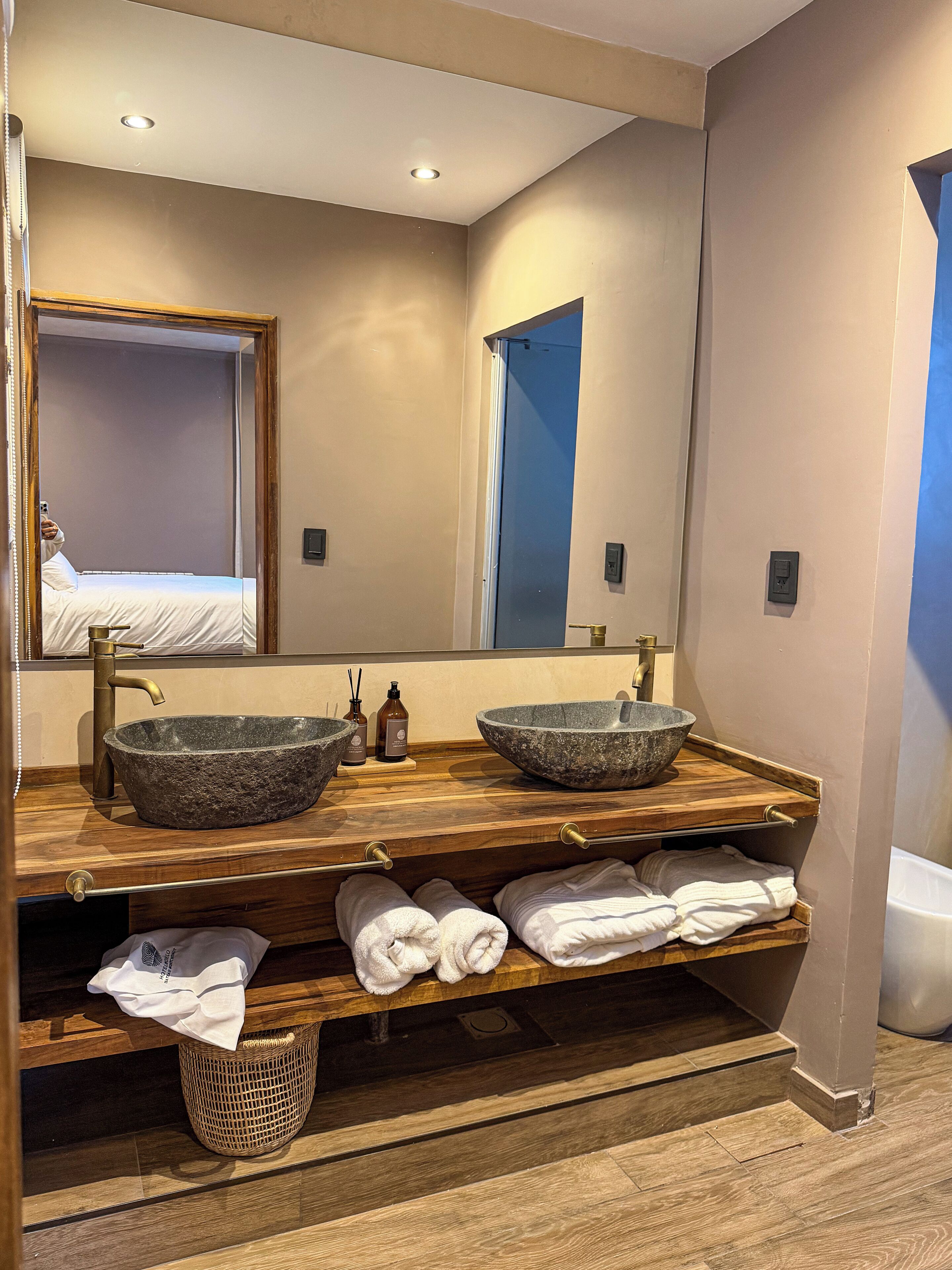 Une salle de bain avec deux vasques en pierre, un meuble-lavabo en bois et un miroir.