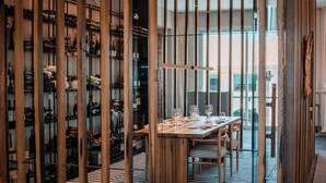 Un restaurante con una mesa de madera preparada para comer, una estantería para vinos y un suelo a rayas.