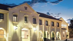 Un edificio grande y bien iluminado con múltiples ventanales arqueados y balcones, un prominente emblema de águila y un letrero que dice 'Sedes Loppz'.