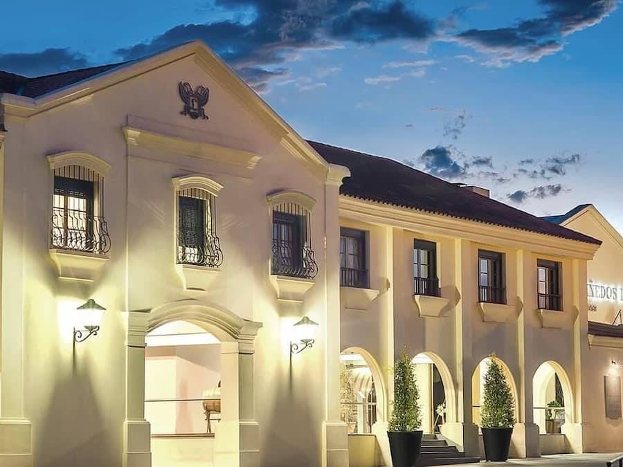 Un edificio grande y bien iluminado con múltiples ventanales arqueados y balcones, un prominente emblema de águila y un letrero que dice 'Sedes Loppz'.