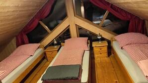 Une chambre mansardée de forme triangulaire, avec deux lits, un plancher en bois et une grande fenêtre.