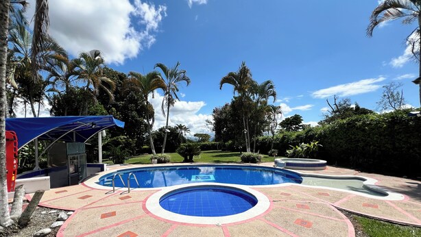 Una piscina dal design circolare, circondata da un'area verdeggiante con palme e un cielo azzurro terso.