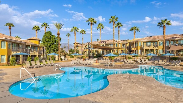 Un hotel con piscina, palmeras y tumbonas.
