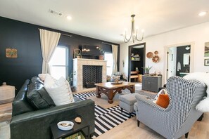 Een moderne woonkamer met een open haard, een zwart-wit gestreept bank en een kroonluchter.
