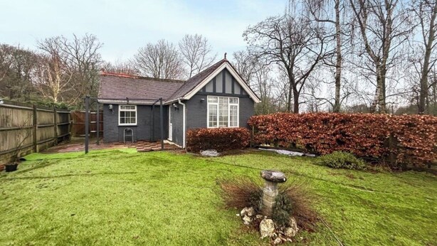 A residential house with a sloped roof, a front yard with a lawn, a wooden fence, and a hedge.