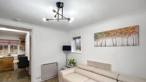 A living room with a beige sofa, a dining area with a table and chairs, a radiator, and a painting on the wall.