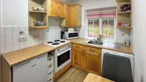 A compact kitchen with wooden cabinets, a microwave, a stove, and a sink.
