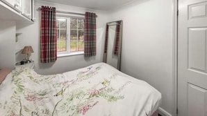 A bedroom with a bed, a window with curtains, a mirror, and a door.
