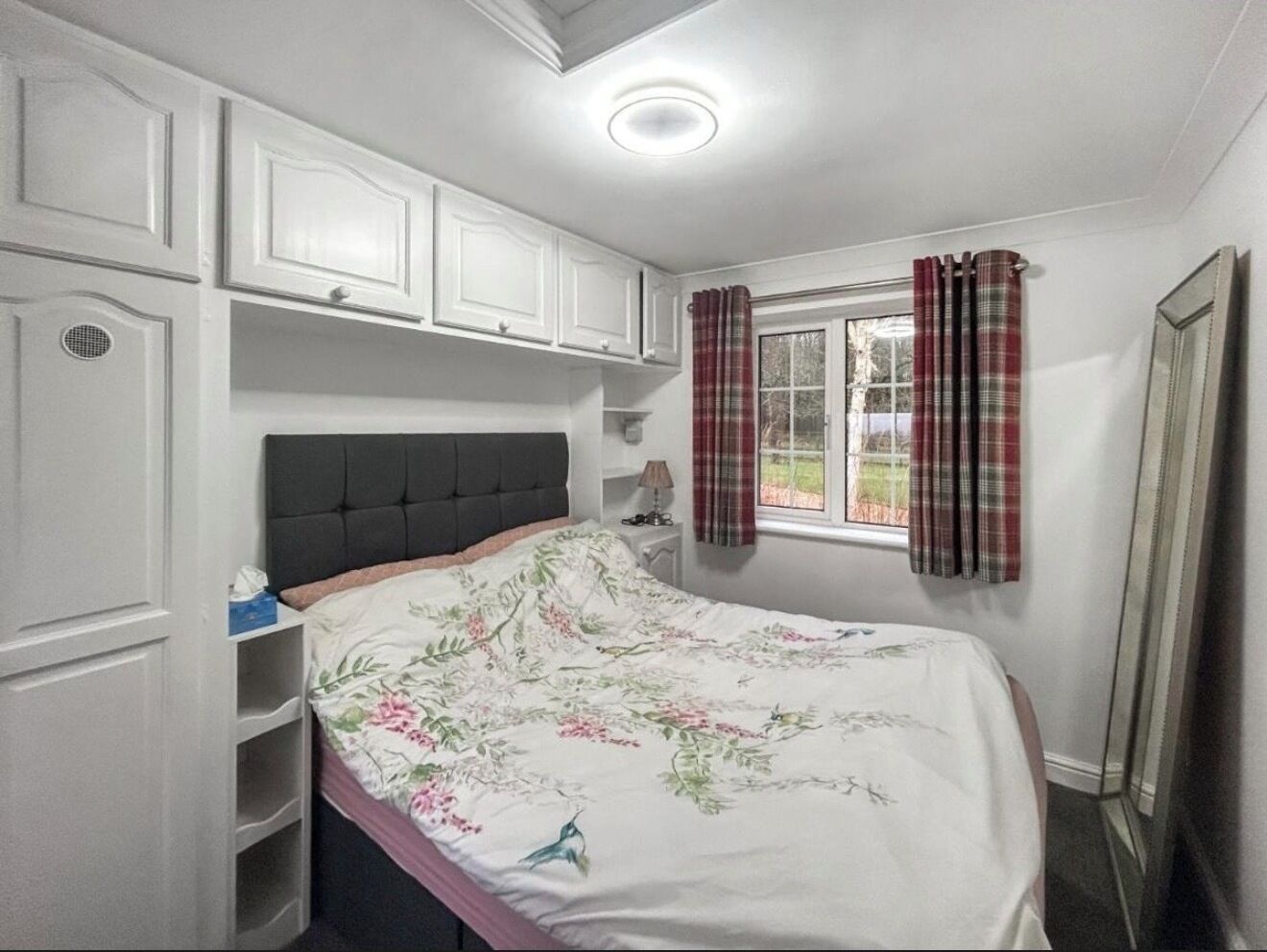 A bedroom with a bed, a window with curtains, a bedside table, and built-in cabinets.