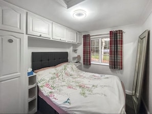 A bedroom with a bed, a window with curtains, a bedside table, and built-in cabinets.