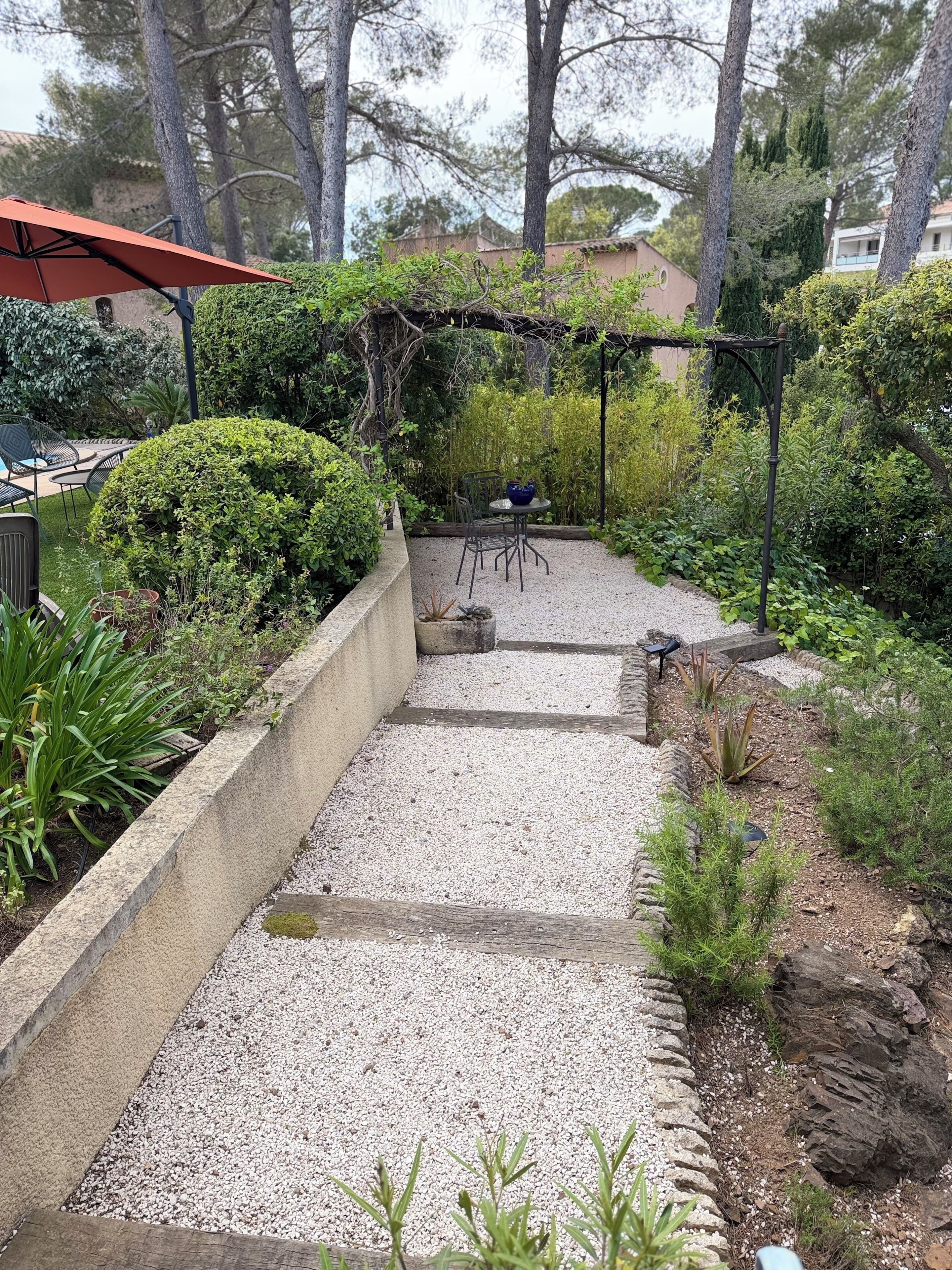 A garden with a gravel path, a pergola, and a seating area with chairs and a table.