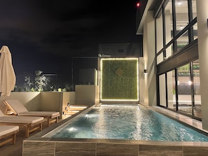Ein Dachpool mit Liegestühlen, eine Wand mit vertikalem Grünbereich und ein modernes Gebäude mit großen Fenstern.