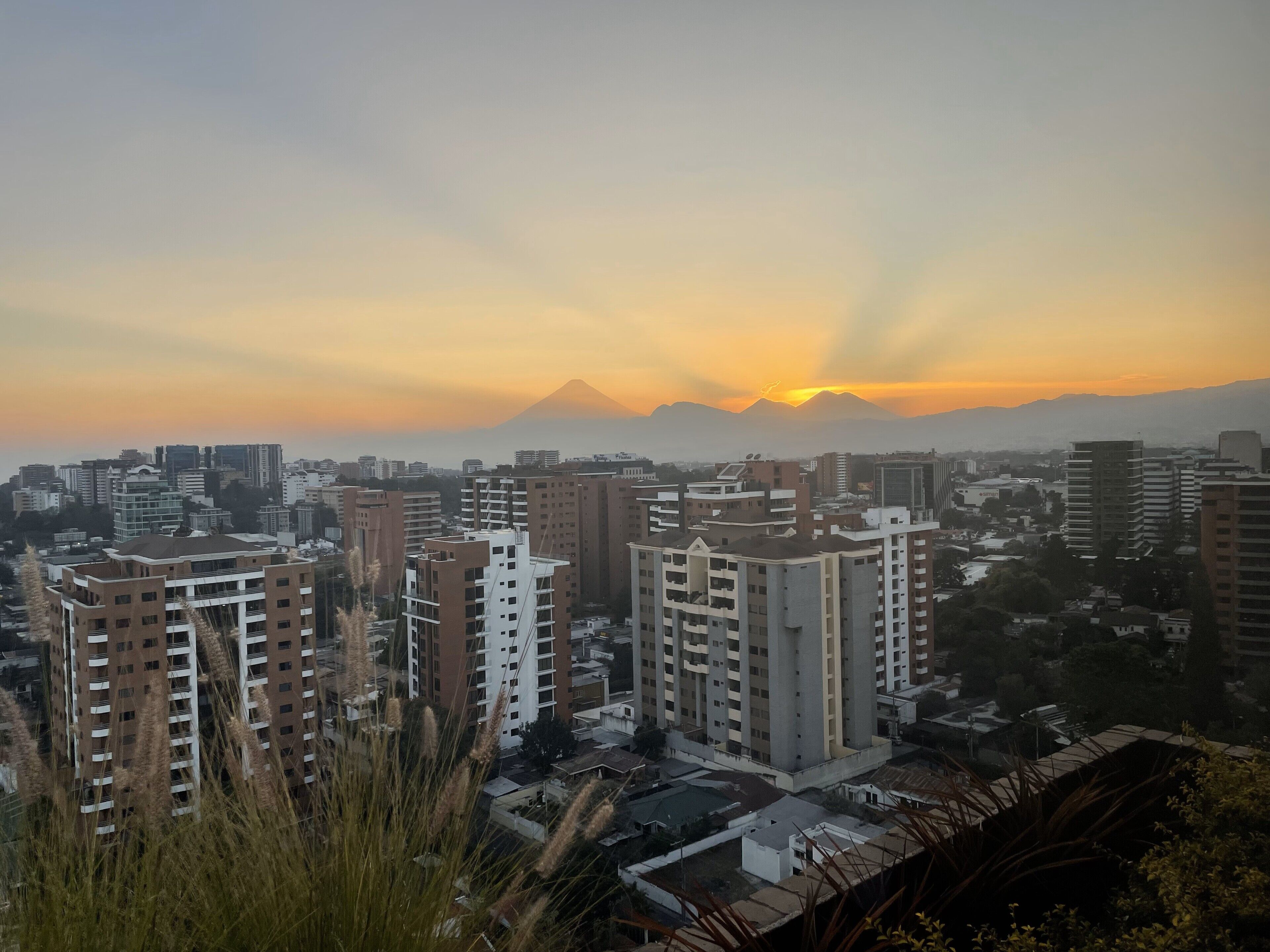 Un paisaje urbano con rascacielos, una montaña al fondo y un atardecer.