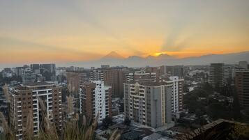 Un paisaje urbano con rascacielos, una montaña al fondo y un atardecer.