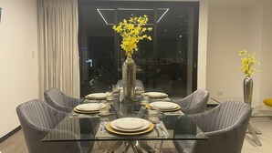 Ein moderner Essbereich mit einem Glastisch, grau gepolsterten Stühlen und einer Vase mit gelben Blumen.