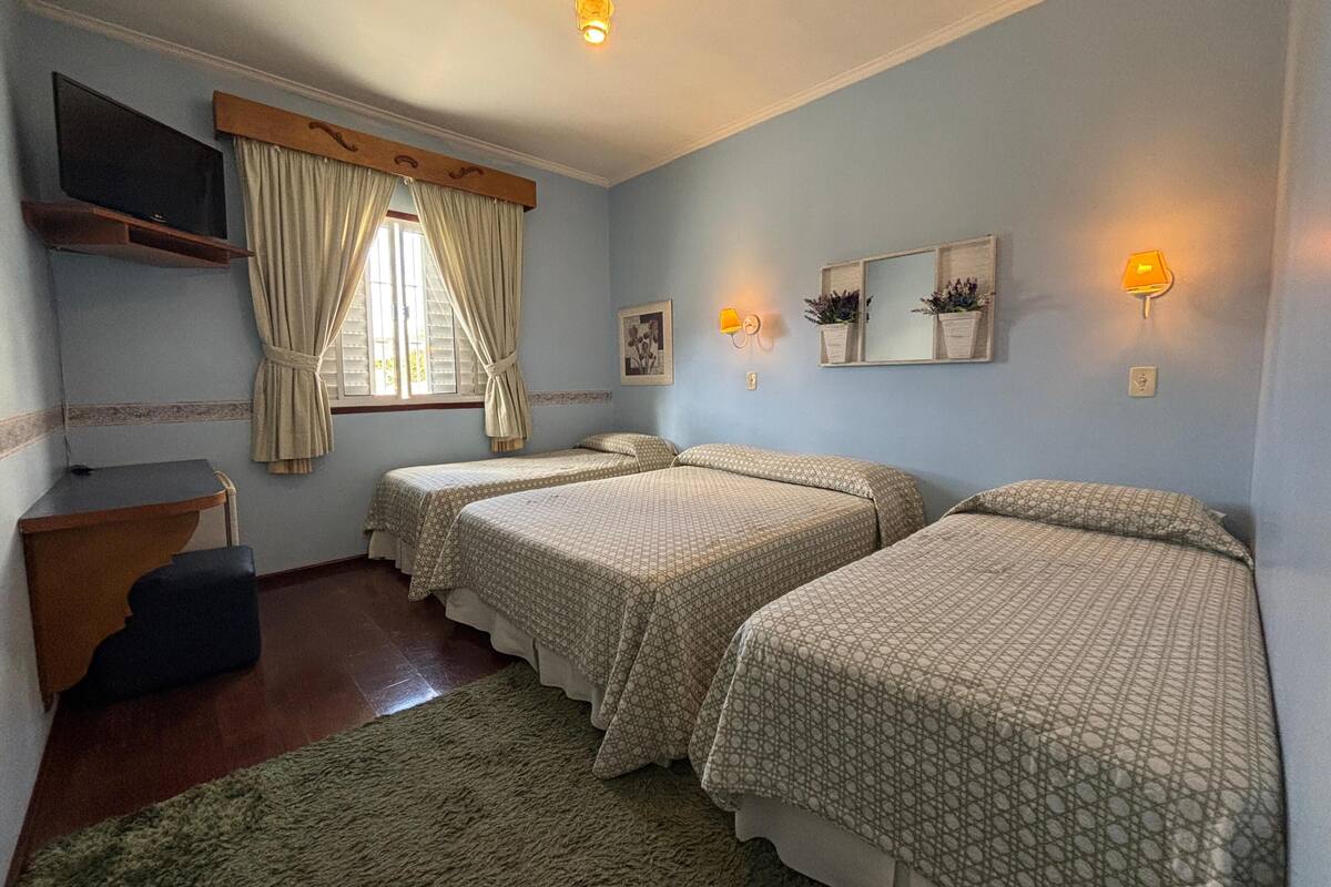 A room with two beds, a desk, a TV, and a window with curtains.