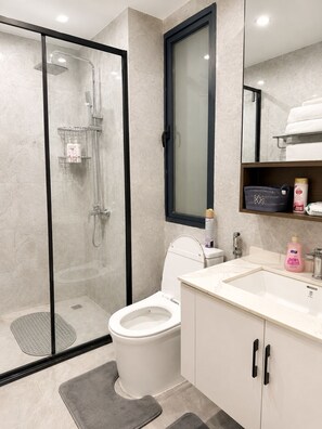 Ein modernes Badezimmer mit einer Duschkabine, einer Toilette, einem Waschbecken mit Spiegel und einem Ablagebereich für Pflegeprodukte.
