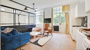 A modern living room with a sofa, a chair, a coffee table, and a TV. There is a kitchen area with a stove and a washing machine. - A REFINED & COMFORTABLE BASE IN D MOST CAPTIVATING NEIGHBOURHOODS-SAINT GERMAIN (Paris)