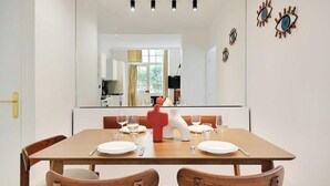 A dining area with a wooden table, four chairs, and a red decorative piece. - A REFINED & COMFORTABLE BASE IN D MOST CAPTIVATING NEIGHBOURHOODS-SAINT GERMAIN (Paris)