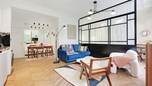 A modern living room with a blue sofa, a white armchair, a wooden coffee table, and a black-framed wall unit. - A REFINED & COMFORTABLE BASE IN D MOST CAPTIVATING NEIGHBOURHOODS-SAINT GERMAIN (Paris)