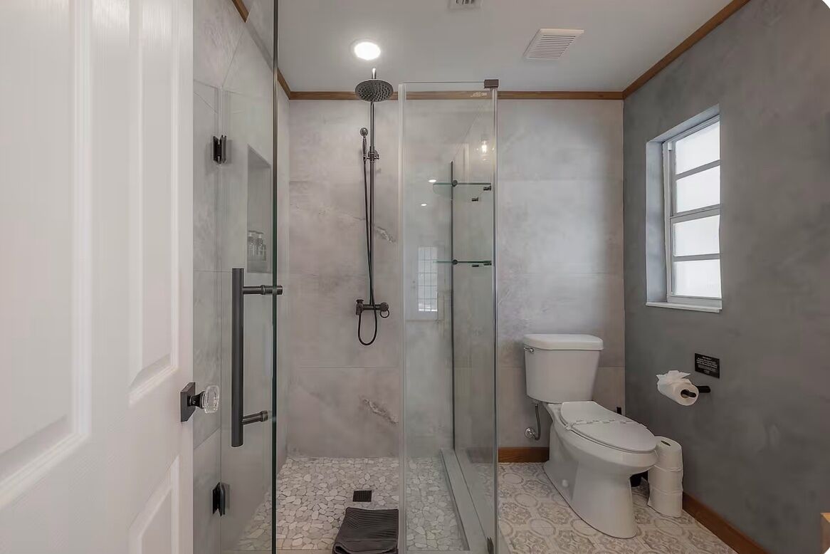 A bathroom with a glass-enclosed shower, a toilet, and a window.