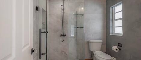 A bathroom with a glass-enclosed shower, a toilet, and a window.