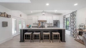 Cozinha moderna com ilha central, banquetas, armários brancos e um lustre.