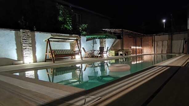 An outdoor swimming pool with a wooden deck, lounge chairs, and a small table.