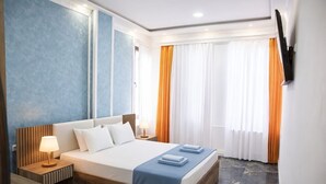 A hotel room with a bed, a nightstand, a TV mounted on the wall, and a window with curtains.