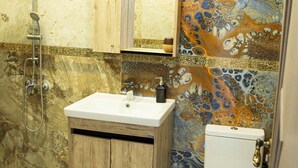 A bathroom with a shower, sink, and toilet, featuring a marble wall and a colorful mosaic backsplash.