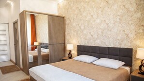 A hotel room with a large bed, a wardrobe, a nightstand with a lamp, and a textured wall.