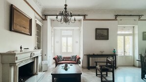 A spacious living room with a fireplace, a chandelier, a sofa, and a dining table. - Unique sunlit house overlooking the Acropolis (Athina)