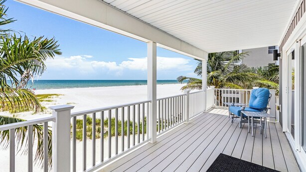 A covered porch with a view of a beach, white railings, and a blue chair. - Island Girl vacation Home (Fort Myers Beach)