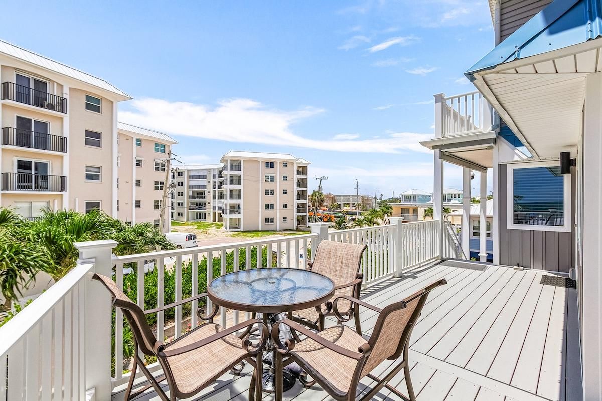 A balcony with a round table and chairs, overlooking a residential area with multi-story buildings.