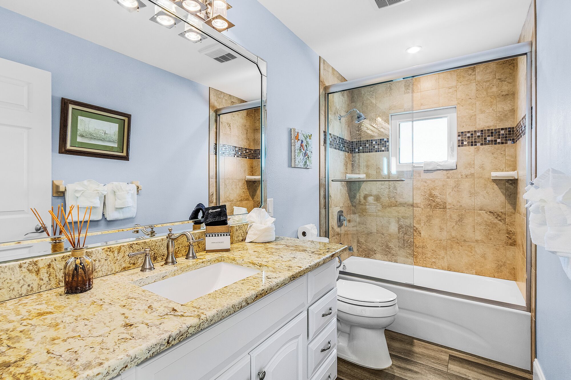 Une salle de bain dotée d’un comptoir en granit, d’un lavabo blanc, de toilettes et d’une douche à parois de verre.