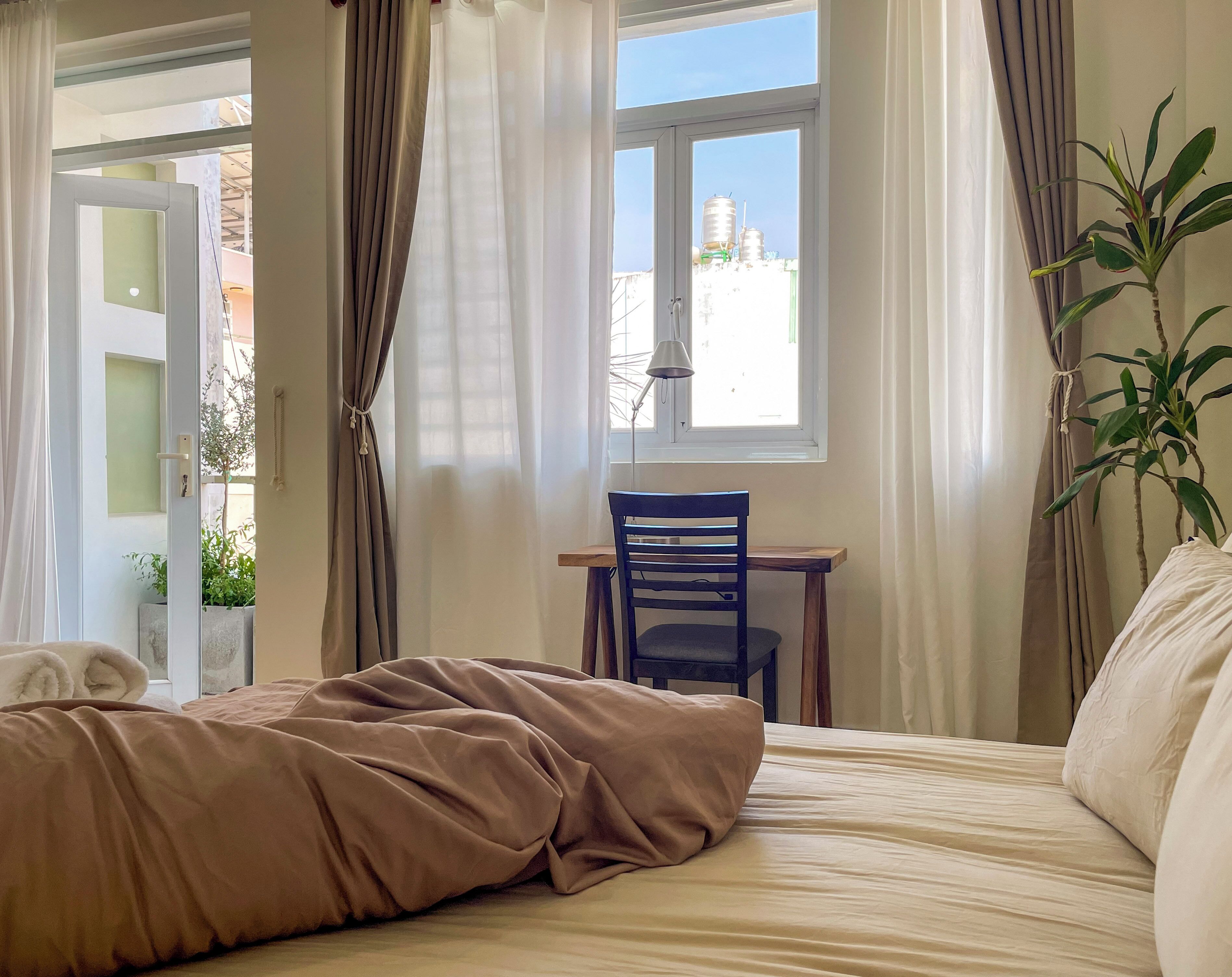Un dormitorio con una cama, una silla, una mesa y una ventana con cortinas.