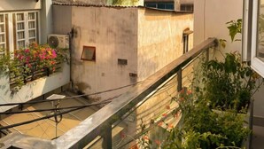 Un edificio residencial de varios pisos con balcones, un equipo de aire acondicionado visible y macetas con plantas.