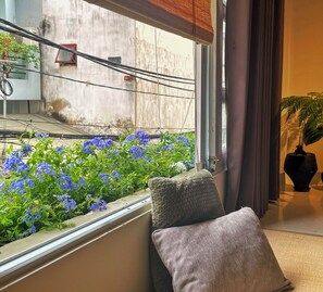A room with a window overlooking a balcony with blue flowers, a cushion, and a potted plant. - Kén Stay  (Phu Nhuan)