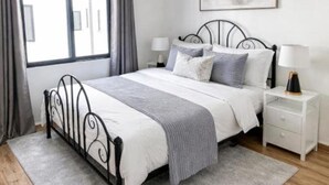 A bedroom with a bed, bedside tables, a window, and a painting on the wall. - GL Luxe Suites 2-bedroom apartment in Tatu City (Tatu City)
