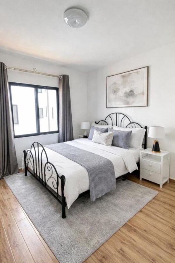 A bedroom with a bed, bedside tables, a window, and a painting on the wall.