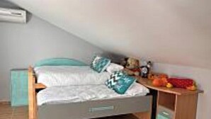 A single bed with a headboard, a bedside table with a lamp, and a small shelf with items.