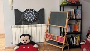 A room with a dartboard, a small easel with a chalkboard, a bookshelf, a plush toy, and a play mat.